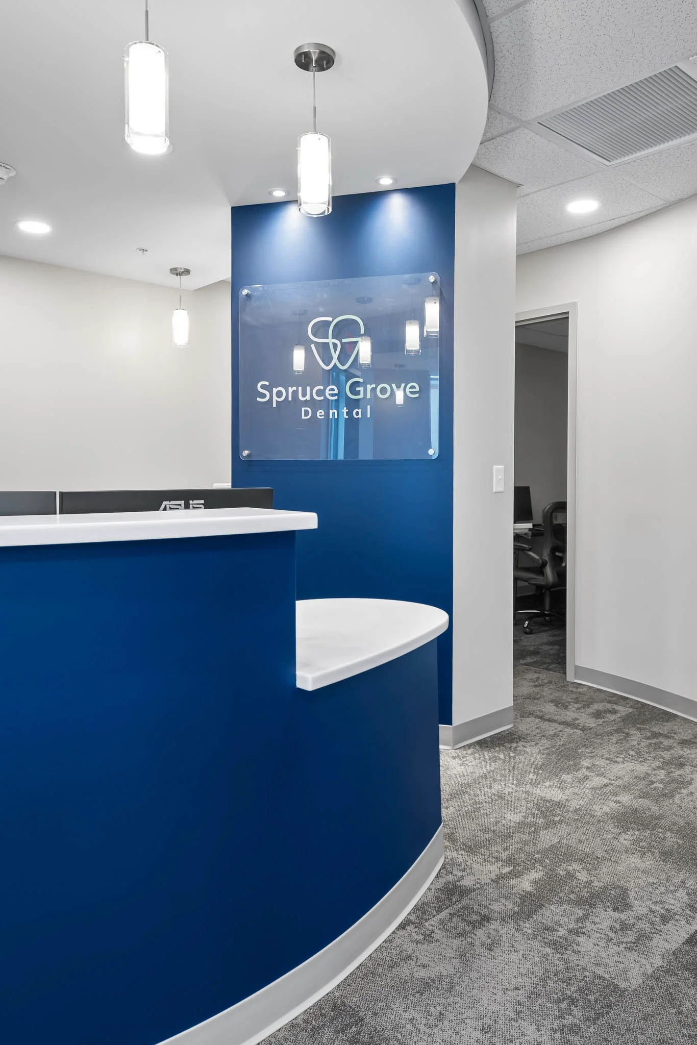 Curved blue reception desk and Spruce Grove Dental logo wall