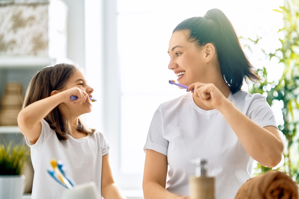 Mother and daughter smiling while brushing their teeth