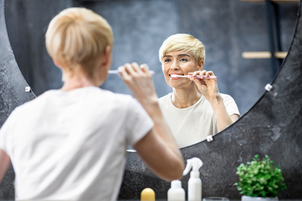 Woman brushing her teeth while looking in a bathroom mirror